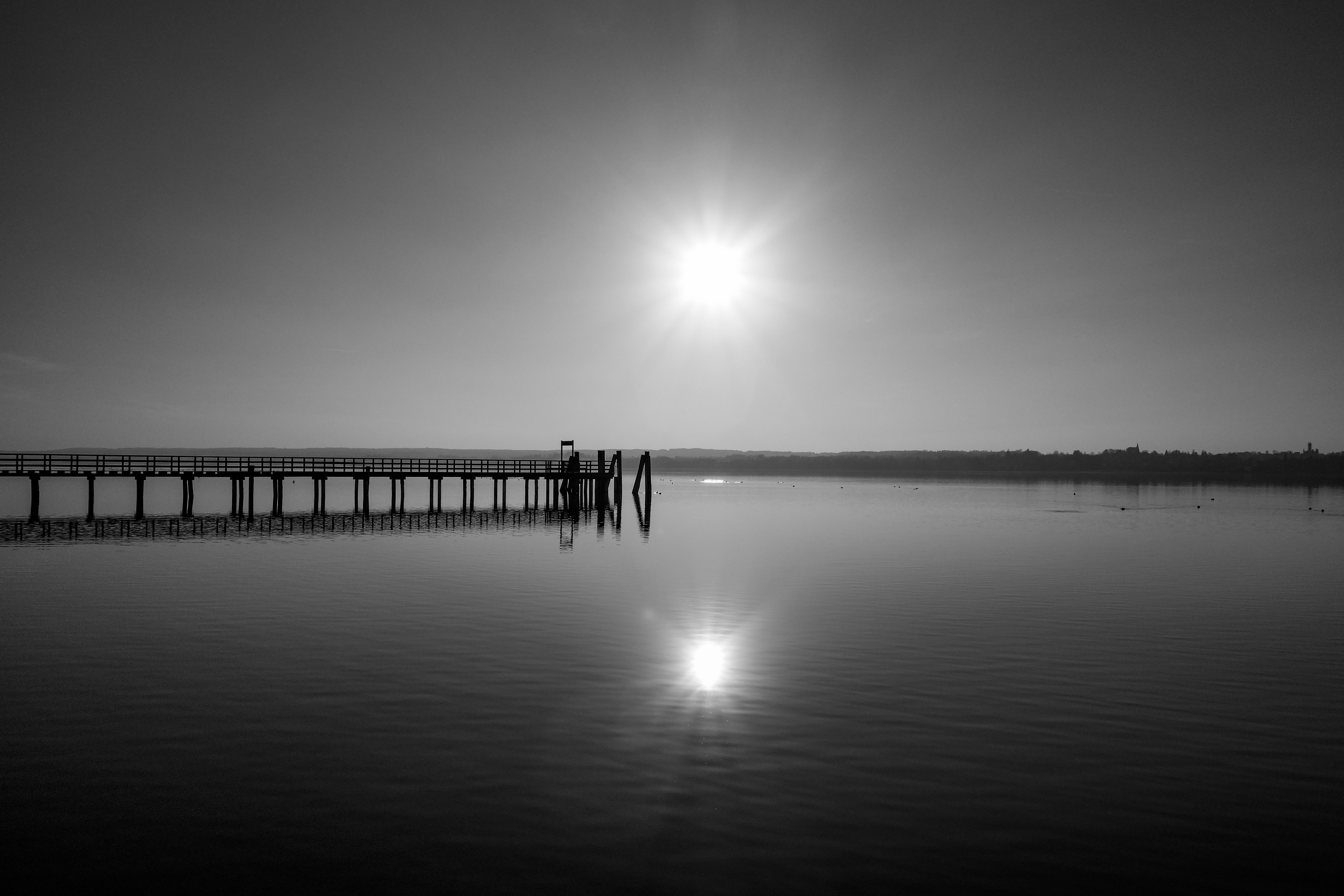 Blick auf einen Steg am ruhigen Wasser bei Sonnenuntergang, schwarz-weiß. Im Seelenblick Coaching Diane K. Senft