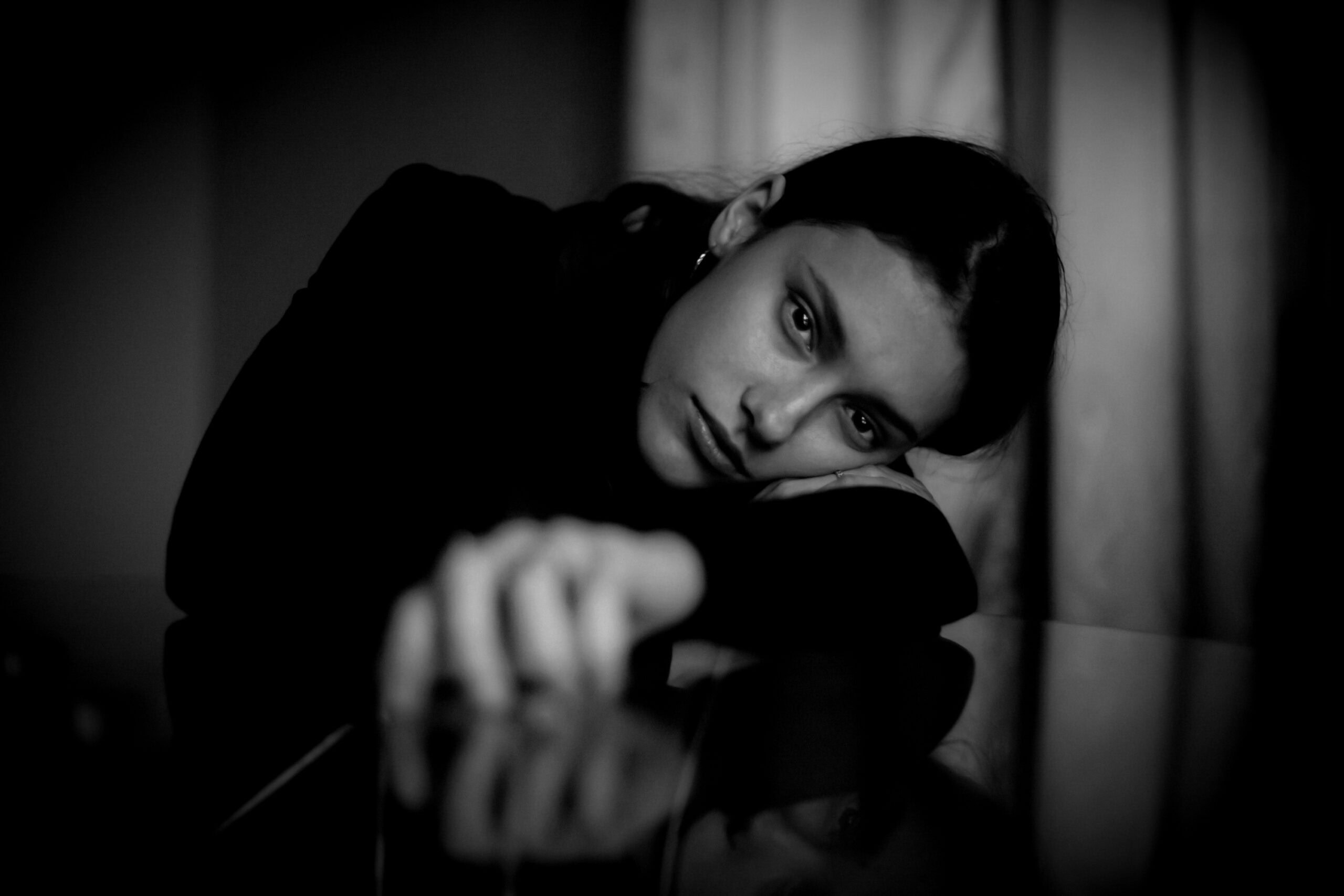 Nachdenkliche Frau in Schwarz-Weiß, die auf einem Tisch liegt und direkt in die Kamera schaut. Porträtfotografie Diane K. Senft