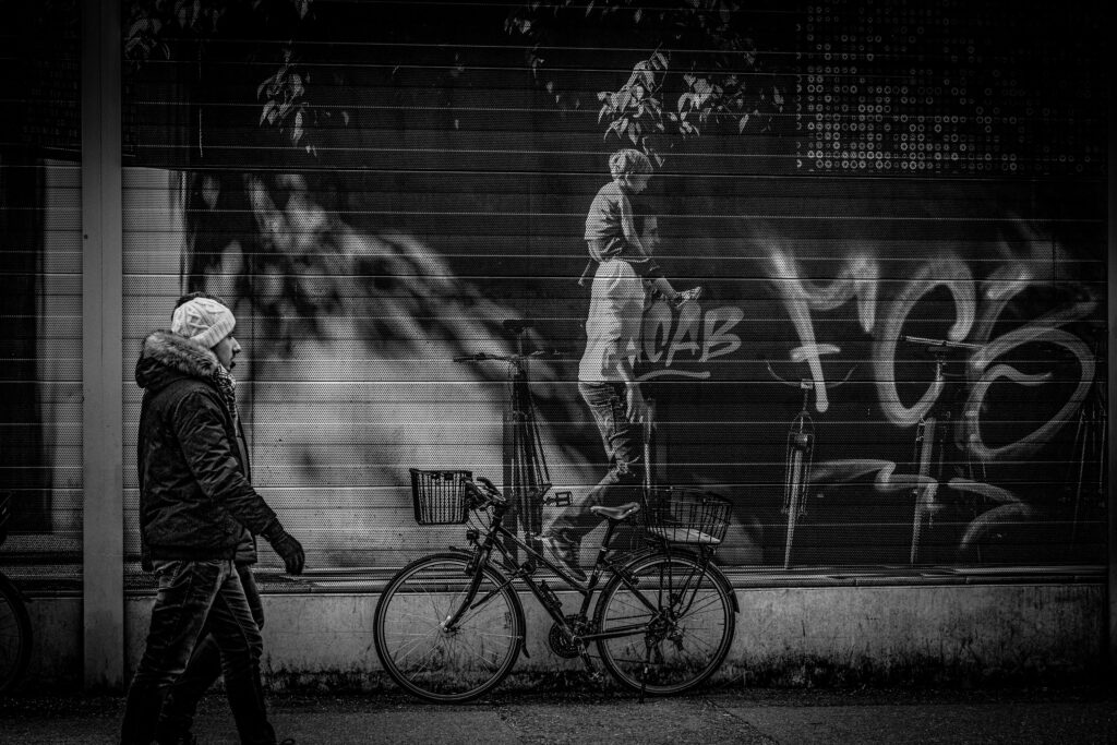 Menschen auf der Straße bei Nacht, Graffiti an der Wand, Fahrrad im Vordergrund.