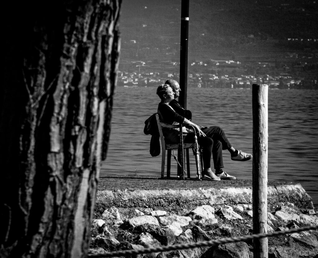 Frau sitzt am Wasserufer auf einer Bank, Blick auf den See, ruhige Atmosphäre.