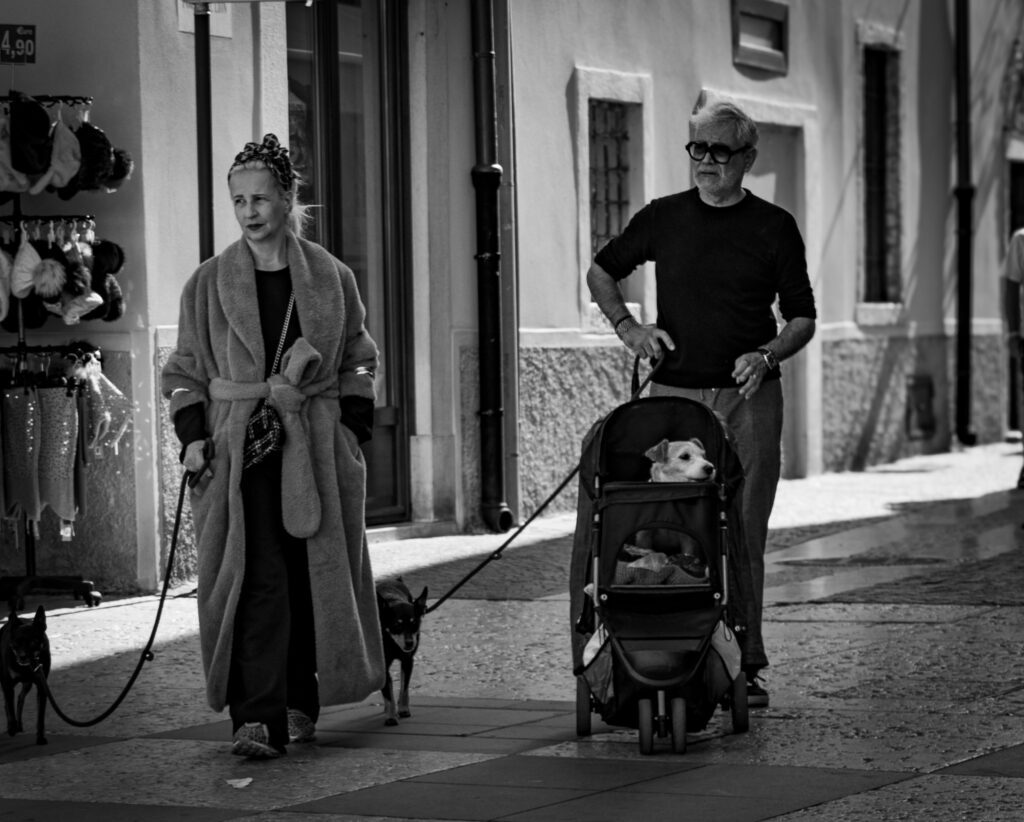 Frau und Mann mit Hund auf Stadtstraße von Lazise unterwegs. Streetfotografie Diane K. Senft