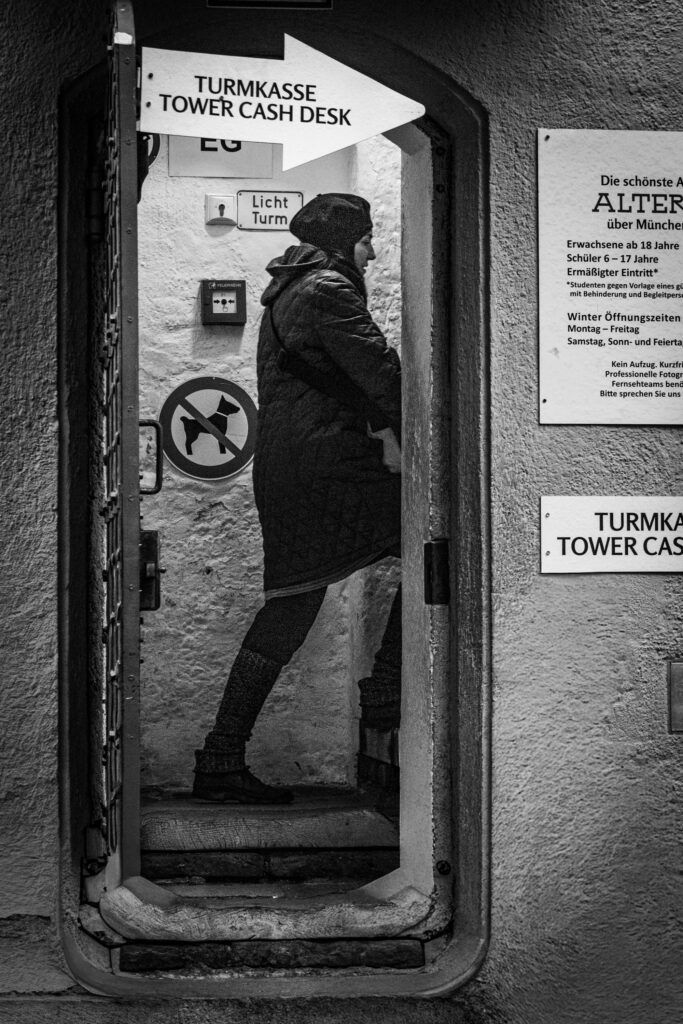 Frau steht in Türöffnung zum Aufstieg auf einen Kirchturm in München, Blick nach rechts, Stadtumgebung, Streetfotografie
