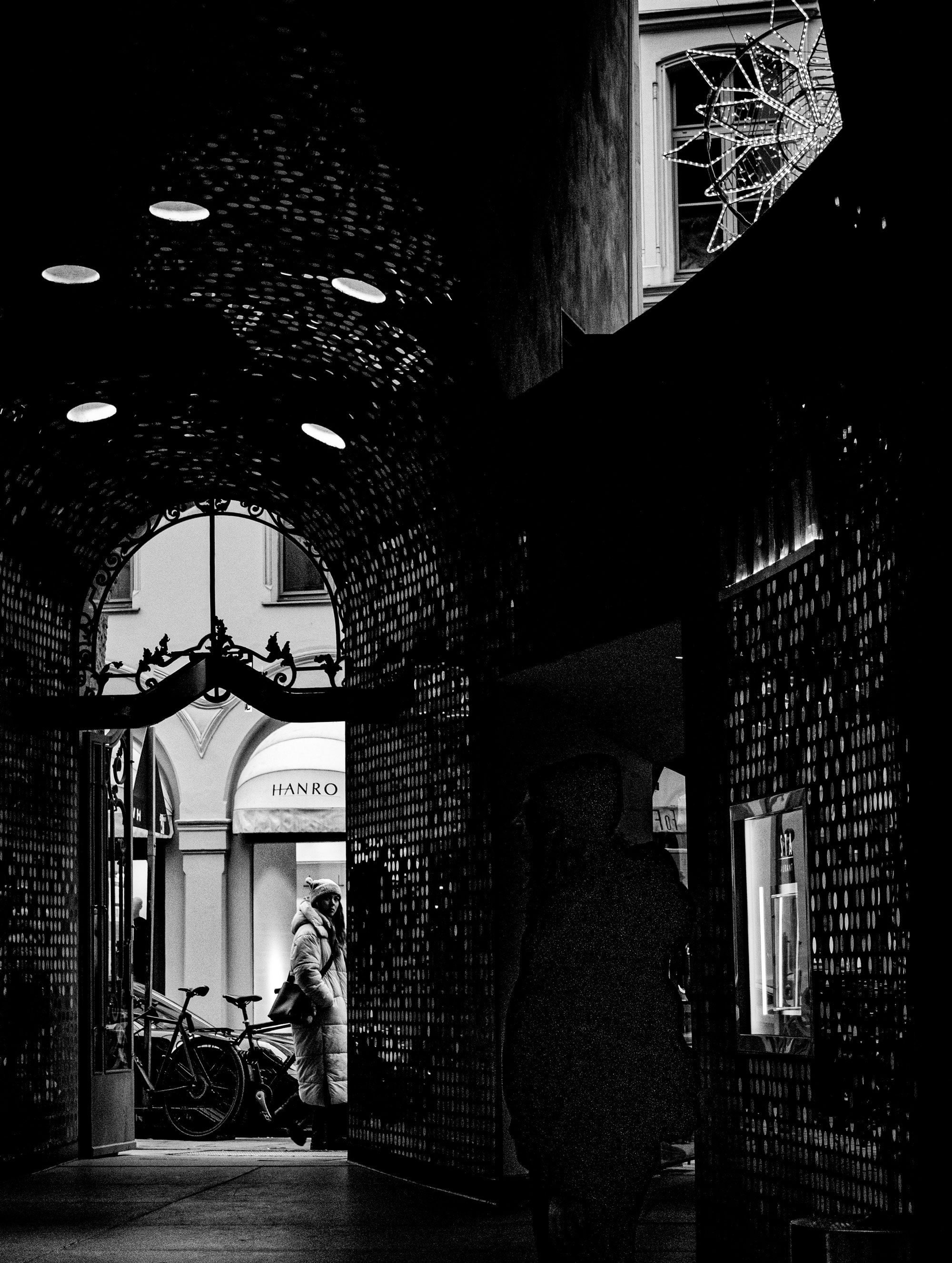 Dunkle Einkaufspassage mit Bogen und beleuchteten Fenstern bei Nacht.