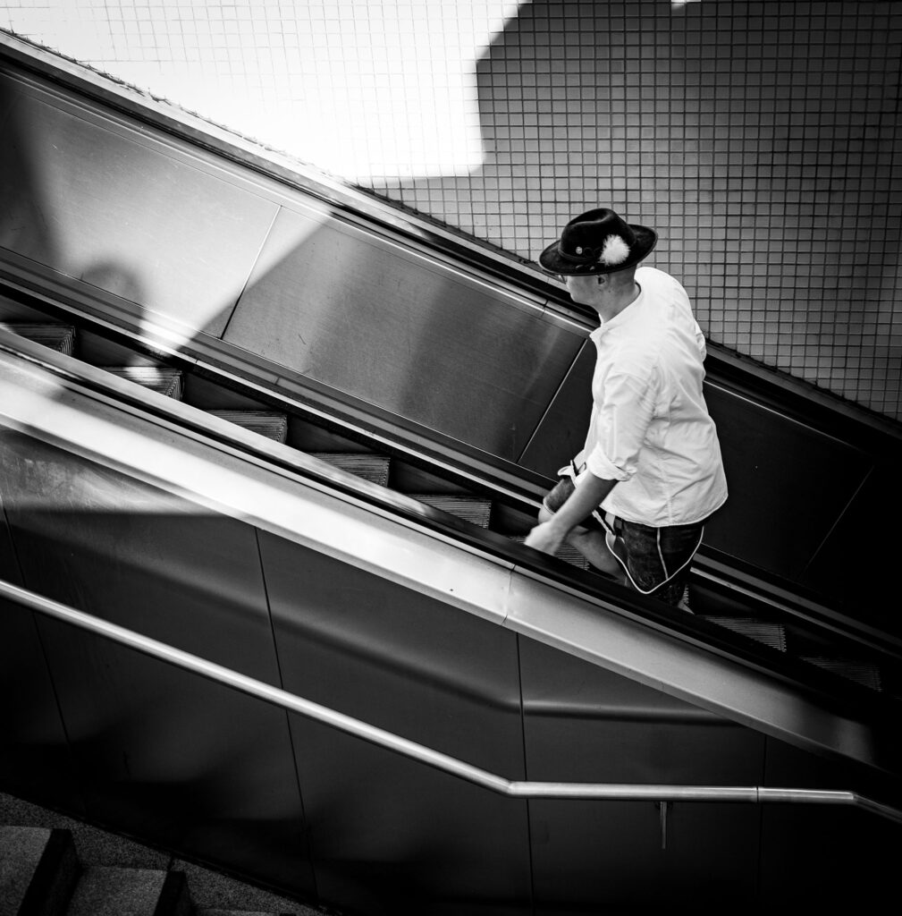 Person auf Rolltreppe in Stadt, moderne Architektur im Hintergrund.